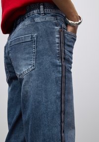 Pantalones de mezclilla azul oscuro con un corte relajado, que presentan un diseño de raya lateral, cintura elástica y bolsillos traseros.