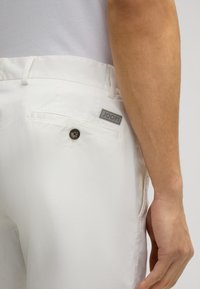 White trousers made from lightweight material, featuring a back pocket with a button and a small grey "JOOP!" label. Smooth texture.