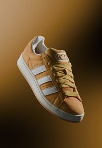 Suede sneakers in light orange with white stripes, round logo, and yellow laces. Features a thick white rubber sole.