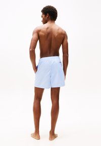Shorts de bain bleu clair en tissu à séchage rapide, avec une taille élastique et des poches latérales, affichant un design uni sans motifs visibles.