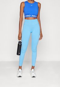 Blauw sportcroptop met contrasterende witte "PRO NIKE" band, gecombineerd met lichtblauwe leggings. Zwarte waterfles, witte sneakers.