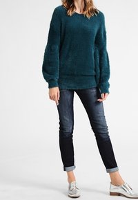 Turkos fluffig tröja med långa, lösa ärmar, i kombination med mörka denimjeans som är uppvikta i fållarna och silverfärgade snörskor. Enkel och mysig design.