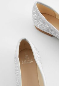 Silberne Ballerinas aus strukturiertem Stoffobermaterial, verziert mit kleinen Strassteinen und einer glatten beigen Innensohle. Weiches, abgerundetes Design.