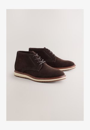 Pruunid seemisnahast pahkluu saapad ümarate esiosade, paeltega esikülje, valge keskmise tallaga ja pruuni kummist tallaga. Külgedel peened õmbluse detailid.