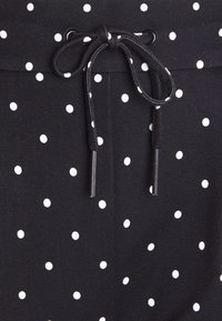 Svarta byxor i tyg med vita prickar, resårmidja och snörning med svarta spetsar för justering.