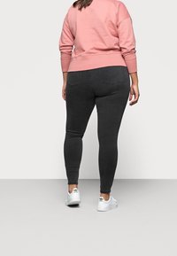 Czarne skinny jeans z tylnymi kieszeniami, w zestawie z różową bluzą. Białe sneakersy z czarnymi akcentami dopełniają outfit.