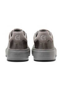 Šedé kožené tenisky s semišovými akcenty, polstrovaným límcem a gumovou podrážkou. "COLE HAAN" je vyraženo na patě a logo je na zadní části.