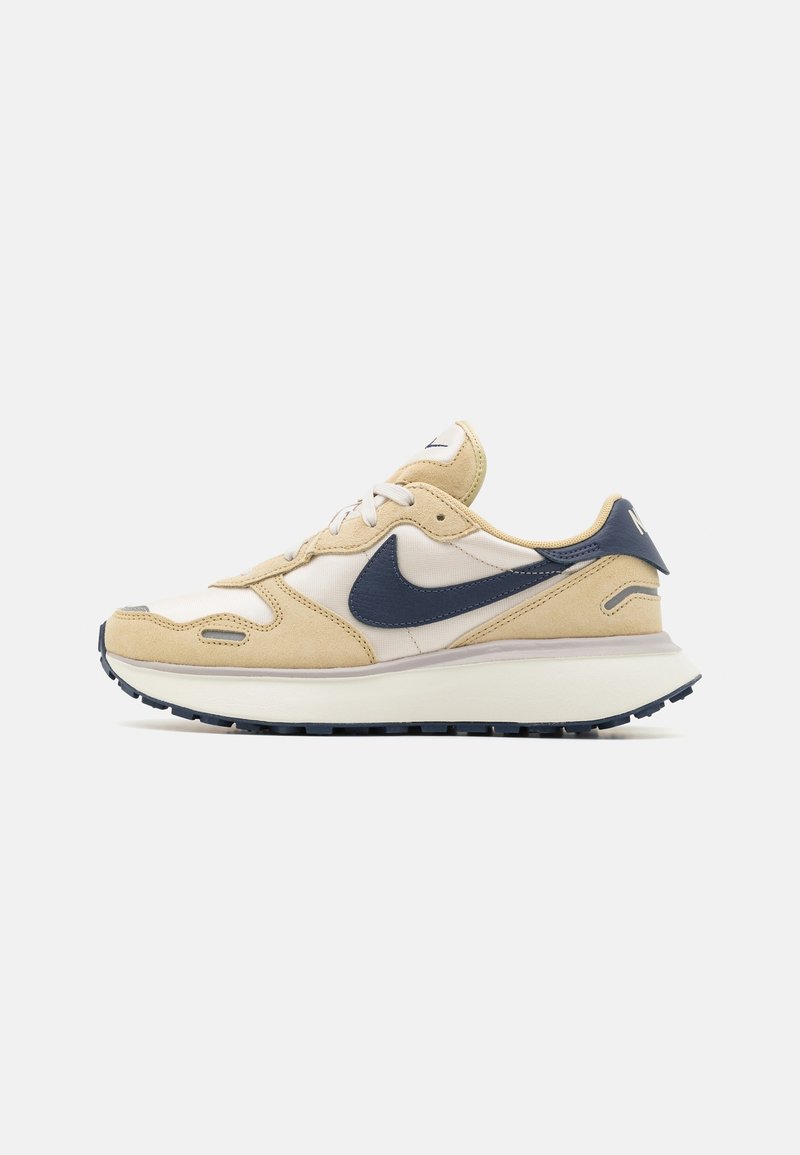 Beige suede and fabric sneaker with navy accent, white swoosh logo, and a textured rubber outsole. Featured layered design and cushioned sole.
