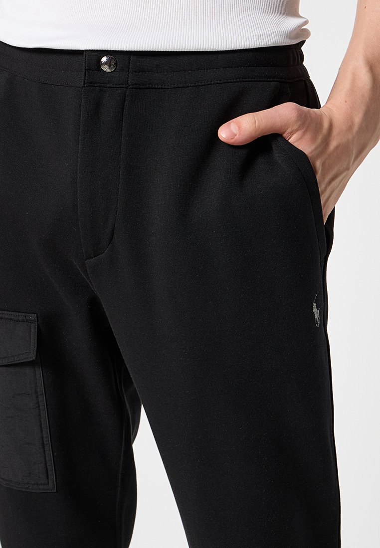 Czarne spodnie cargo wykonane z miękkiego, elastycznego materiału. Posiadają kieszeń z przodu, elegancki fason oraz mały akcent z logo w pobliżu pasa.