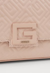 Sac bandoulière en cuir rose blush avec un motif géométrique matelassé, présentant un logo en forme de G bien visible et le marquage doré "GUESS".