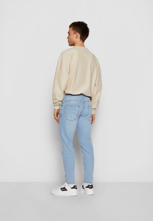Beige pitkähihaine paita, jossa on ribbikuvio, vaaleansiniset slim-fit farkut ja valkoiset tennarit mustilla yksityiskohdilla. Näkymä takaa.