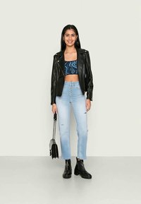 Jaqueta de motoqueiro em couro preto, crop top azul com padrão, jeans de cintura alta em azul claro com fecho de botão, e botas pretas até o tornozelo.