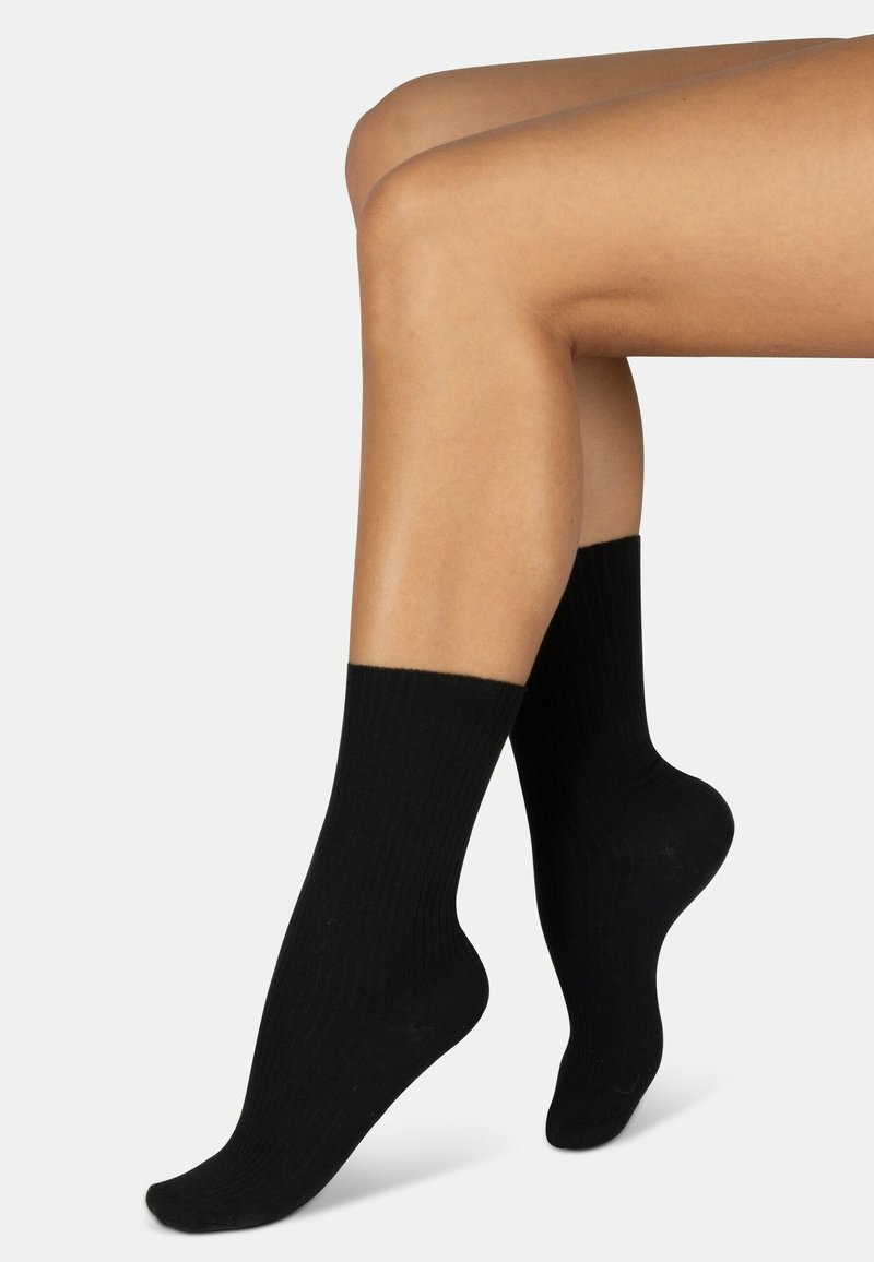 Schwarze Rippensocken bis zum Knöchel aus einem weichen Material, mit einem glatten Bund und einer standardmäßigen Form. Der Stoff wirkt dehnbar und bequem.