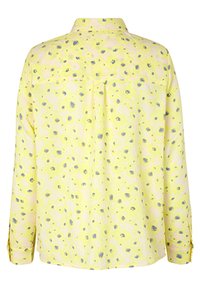 Gul bluse med blomstermønster i grå, med krave med knaplukning, lange ærmer og en afslappet pasform. Inkluderer bagfoldningsdetalje.