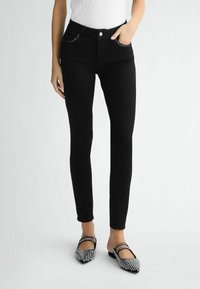 Jean skinny noirs à taille haute, design à cinq poches, détails de couture subtils et texture lisse, associés à des ballerines ornées.