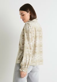 Blusa de manga larga con un patrón abstracto en beige claro y blanco, mangas fruncidas con puños con volantes y un escote alto.