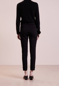 Schwarze Slim-Fit-Hosen mit tailliertem Design, ausgestattet mit Gesäßtaschen und umgeschlagenen Säumen, kombiniert mit einem engen schwarzen Langarmoberteil.