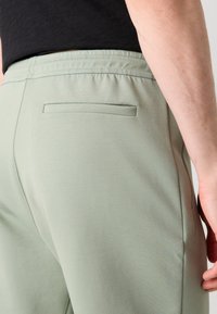 Svetlozelené jogger nohavice vyrobené z jemného materiálu, s elastickým pásom, jednou zadnou vreckom a hladkou textúrou.