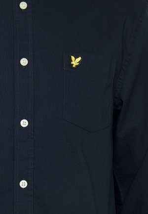Navy button-up shirt made of cotton, featuring a chest pocket with an embroidered yellow eagle logo and light-colored buttons.