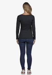 Schwarzes langärmliges Oberteil mit einem gewellten Halsausschnitt, kombiniert mit dunkelblauen Jeans und weißen Sneakers mit rosa Akzenten.