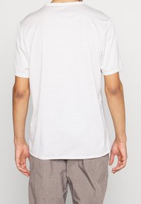 Hvid kortærmet skjorte med subtilt teksturmønster, rund halsudskæring og afslappet pasform. Kombineret med løstsiddende grå bukser.