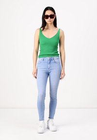 Green ribbed tank top, light blue skinny jeans, white sneakers, and dark sunglasses. Smooth texture and fitted design.
