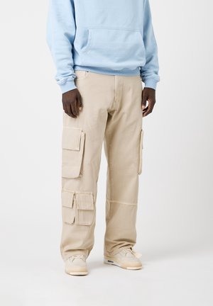 Beige cargobroek met meerdere zijzakken, gemaakt van katoen. Graag gedragen met een lichtblauwe hoodie en beige sneakers. Casual pasvorm, rechte snit.