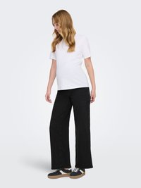 T-shirt bianca a maniche corte abbinata a pantaloni neri a gamba larga e sneaker nere con dettagli beige. Tessuto liscio e vestibilità comoda.