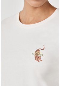 Camiseta de algodón blanca con un gráfico de leopardo en naranja y negro, con texto bordado en verde "SOMMER" cerca del pecho. Cuello redondo.