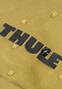Groene textuurstof met in reliëf aangebrachte zwarte letters "THULE". Heldere druppels water op het oppervlak benadrukken de waterbestendigheid.