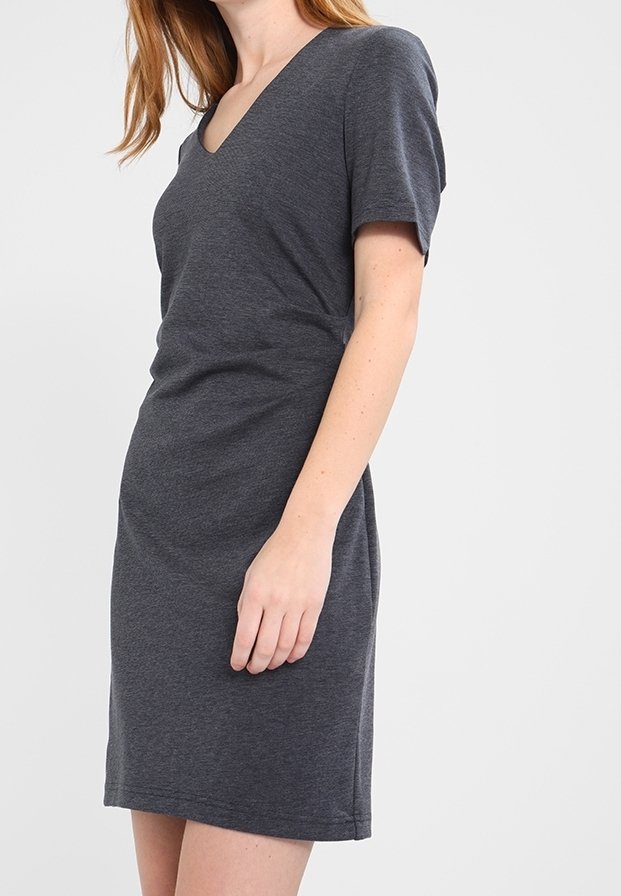 Femme portant une robe cintrée à manches courtes, longueur genou, de couleur gris foncé, avec un col en V, debout sur un fond uni gris clair.