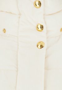 Gilet bianco imbottito con un design trapuntato, bottoni dorati e una texture liscia con dettagli di cucitura visibili.