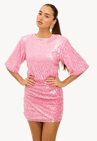 Robe en sequins rose avec des manches courtes, une silhouette ajustée et des détails froncés sur les côtés. Texture lisse avec un aspect brillant.