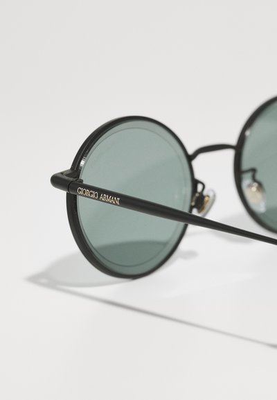 Runda solglasögon med en svart metallram och gröna linser. Har guldaccenter med "Giorgio Armani" på sidan. Minimalistisk design.