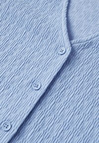 Hellblauer, strukturierter Cardigan mit V-Ausschnitt, der über drei Knopfverschlüsse und ein weiches, gewelltes Stoffmuster verfügt.