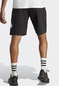Mustat urheilushortsit, jotka on valmistettu pehmeästä kankaasta. Niissä on suora leikkaus, sivutaskut ja logopatch. Yhdistetty valkoisiin ja mustiin raidallisiin sukkiin.
