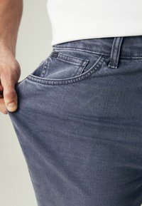 Jeans en denim gris foncé avec une coupe classique, dotés d'une poche avant et d'une couture détaillée le long des coutures. Le tissu semble doux et légèrement usé.