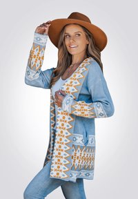 Blauer Cardigan mit komplexen weißen und orangefarbenen Mustern an den Ärmeln und der Vorderseite. Langes, offenes Design mit Taschen, kombiniert mit Jeans.