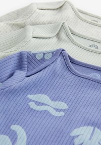 Tre ribbede T-shirts i lys grå, dæmpet grøn og lavendel, med bløde teksturer og subtile farverige mønstre på den lilla skjorte.