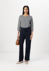 Blusa de rayas de manga larga con escote barco, combinada con pantalones de talle alto en color marino con un cinturón de lazo. Accesorios con un pequeño bolso marrón.