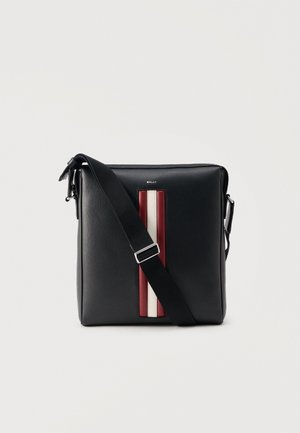 Bolso bandolera Bally negro con una correa ancha ajustable y una franja vertical roja, blanca y roja en la parte delantera, sobre un fondo claro.