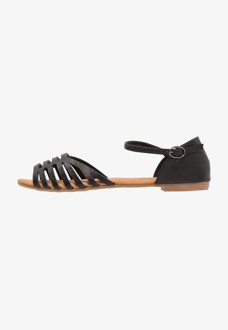 Black sandal with a strappy design, features a flat brown sole, ankle strap with buckle, and a smooth material texture.