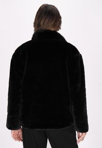 Giacca in pelliccia sintetica nera con una morbida texture, dotata di un collo alto e maniche lunghe. Il design è oversize, offrendo una silhouette rilassata.