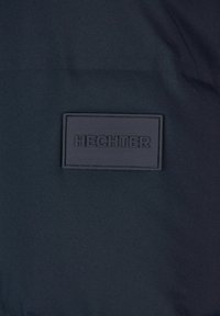 Marinestof med en glat tekstur, der har en rektangulær sort lap præget med "HECHTER." Minimalistisk design uden yderligere mønstre eller accenter.