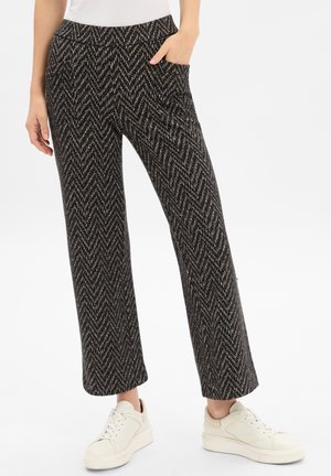 Pantaloni a righe a spina di pesce in bianco e nero con una linea ampia, dotati di tasche frontali. Abbinati a sneakers bianche per un contrasto.