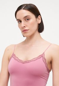 Camisole rose clair avec dentelle le long de l'encolure et bretelles spaghetti réglables, fabriquée dans un tissu doux et extensible.