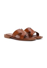 Sandali in pelle marrone con due ampie cinghie e dettagli intagliati, caratterizzati da una suola piatta e una texture liscia, progettati per una facile calzata.