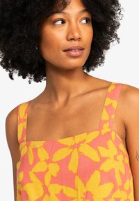 Vestido con estampado floral en rosa y amarillo, con escote cuadrado y tirantes anchos, hecho de tela ligera y con un corte relajado.