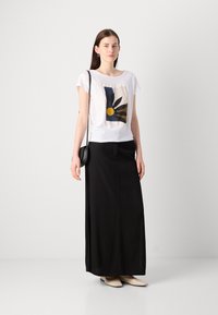 T-shirt blanc avec un graphisme de fleur colorée, associé à une longue jupe noire. Présente une texture lisse et des accents délicats.