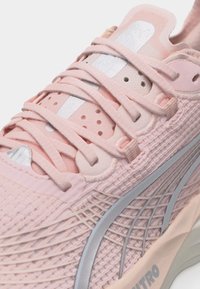 Αθλητικό παπούτσι σε ανοιχτό ροζ χρώμα με πλεκτό επάνω μέρος από δίχτυ, ροζ κορδόνια, ασημένιες ρίγες λογότυπου και μαλακή σόλα με την ένδειξη "NITRO".